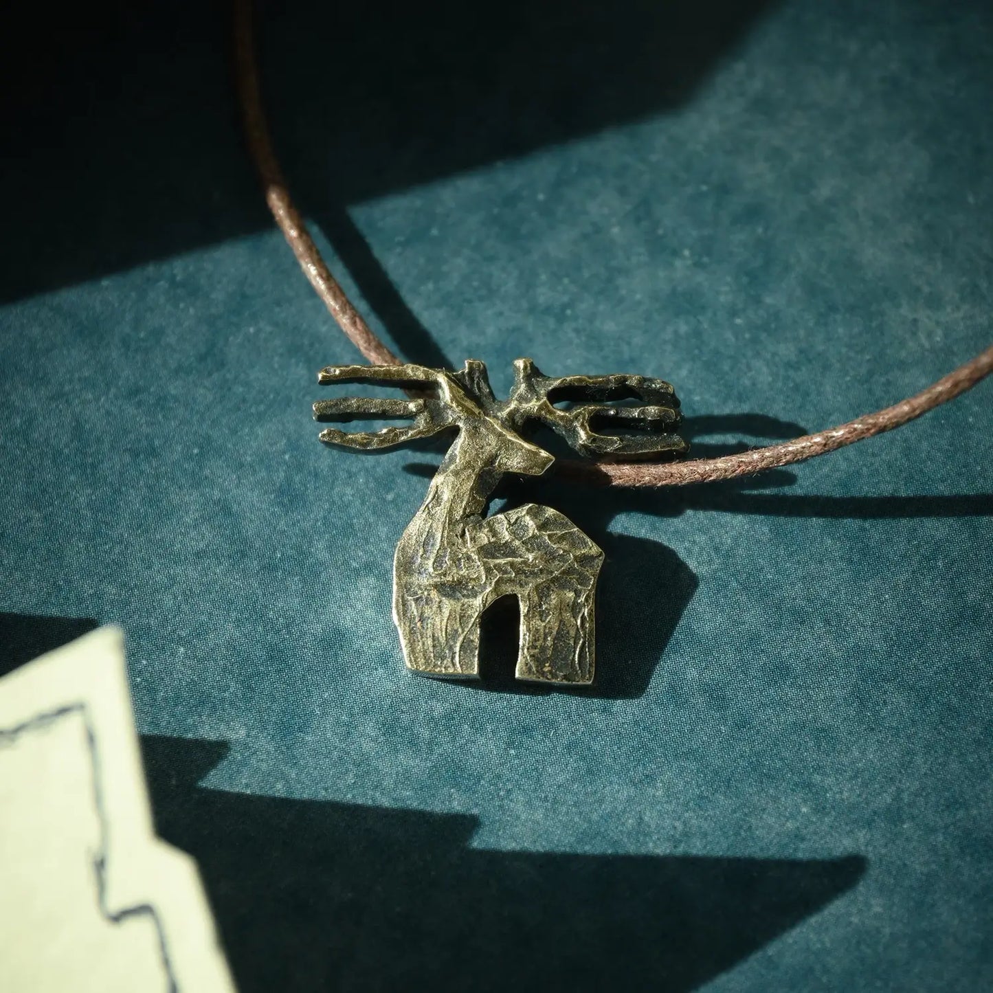 Bronze deer necklace on a brown cord against a teal background