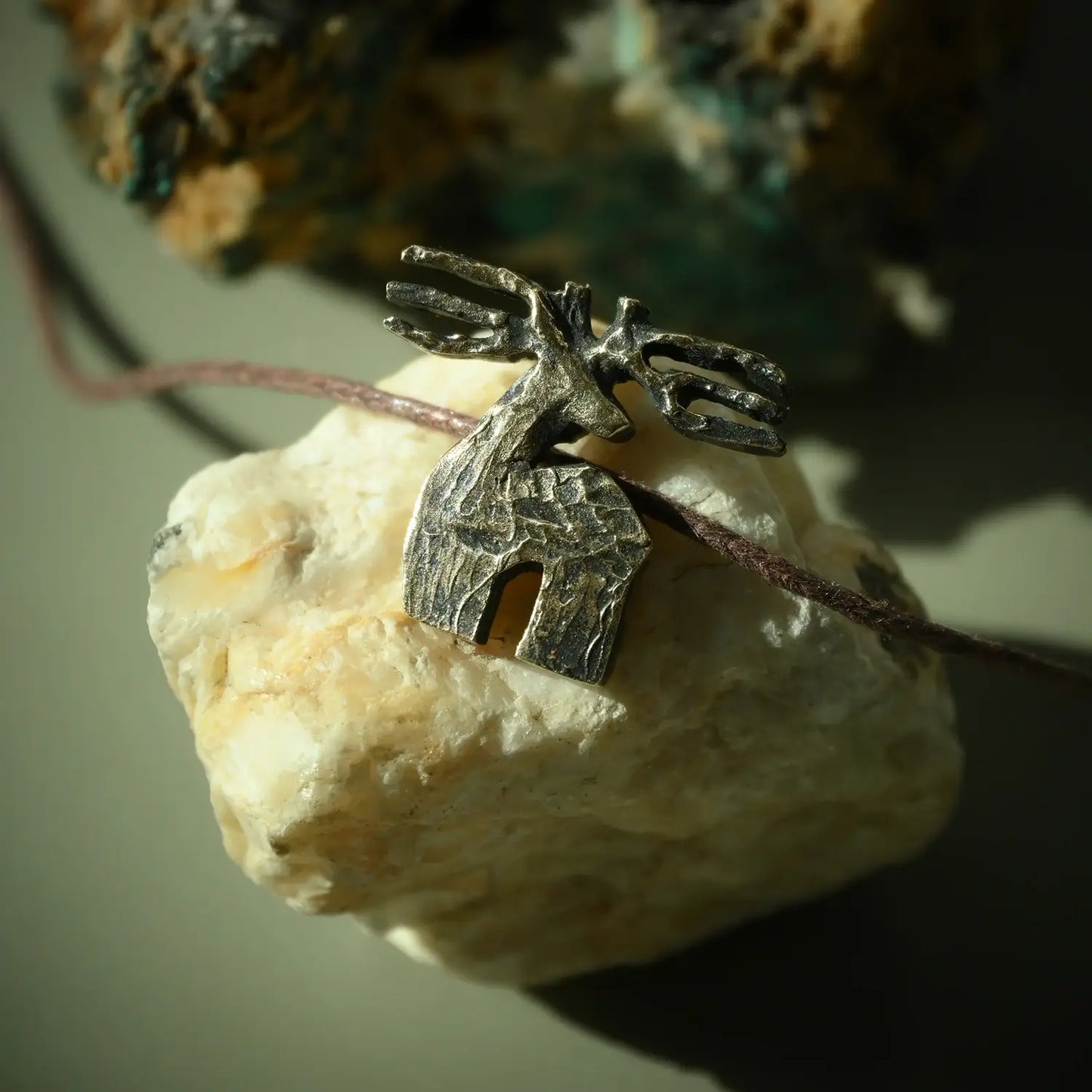 bronze deer pendant on a rock with a blurred natural background